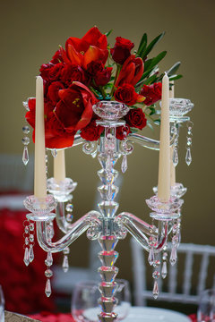 Vertical shot of a romantic formal table centerpiece, a beautiful crystal candelabra style candle holder with eight scalloped bobeche for candlesticks and a red tulips and roses bouquet in the middle