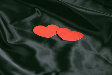 Fototapeta premium two red hearts on a black silk background.