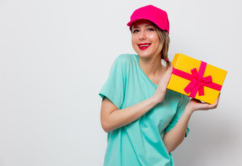 Beautiful young girl in pink cap and blue t-shirt with holiday present box on white background.