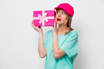 Beautiful young girl in pink cap and blue t-shirt with holiday present box on white background.