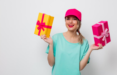 Beautiful young girl in pink cap and blue t-shirt with holiday present boxes on white background.