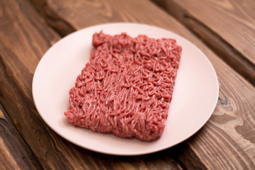 Fresh minced meat on a plate on a wooden background for cooking.