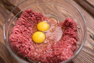 Fresh minced meat with chicken eggs on a plate on a wooden background for cooking.