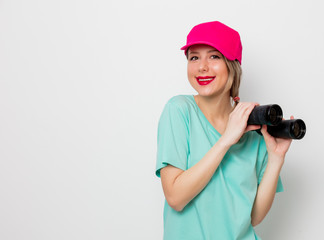 Beautiful young girl in pink cap and blue t-shirt looking for something with binocular on white background.