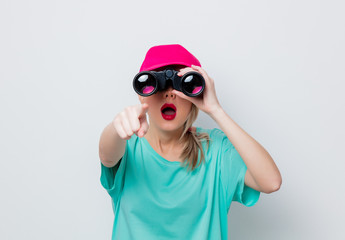 Beautiful young girl in pink cap and blue t-shirt looking for something with binocular on white...