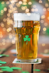 st patricks day, holidays and celebration concept - close up of glass of light beer with shamrock decoration on wooden table