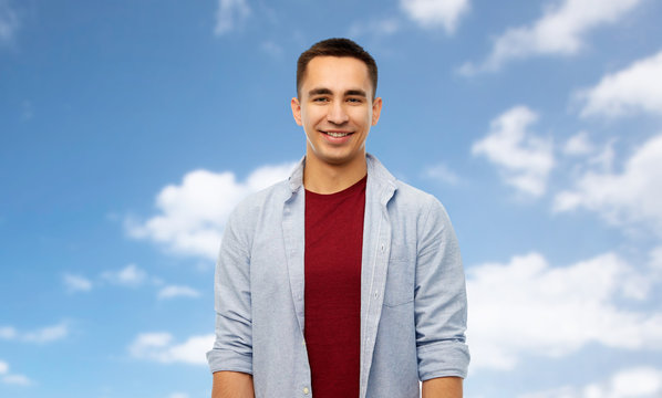 people concept - smiling young man over blue sky and clouds background