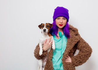 Beautiful young girl with purple hair in jacket holding dog on white background.