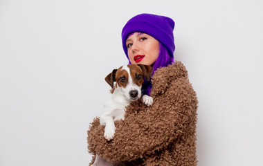 Beautiful young girl with purple hair in jacket holding dog on white background.