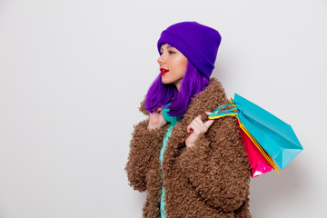 Beautiful young girl with purple hair in jacket holding shopping bags on white background.