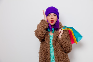 Beautiful young girl with purple hair in jacket holding shopping bags on white background.