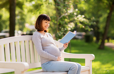 pregnancy, people and motherhood concept - happy pregnant asian woman sitting on park bench and reading book