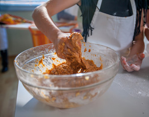 A young girl is kneading dough in a big transparent bowl. She is wearing a white apron. Kids are having a cooking class.