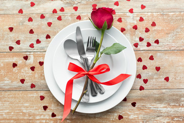 valentines day, table setting and romantic dinner concept - close up of red rose flower on set of dishes with cutlery on wooden background