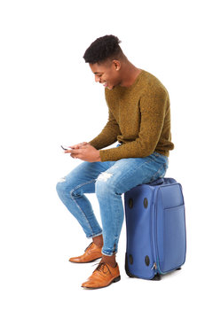 young african american travel man sitting on suitcase with mobile phone