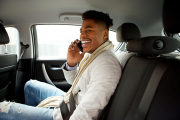 happy young black man sitting in backseat of car and talking with mobile phone