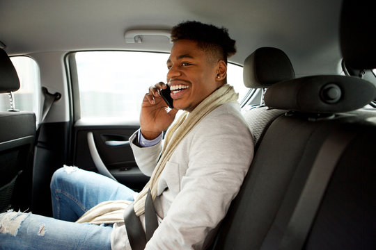 Happy Young Black Man Sitting In Backseat Of Car And Talking With Mobile Phone