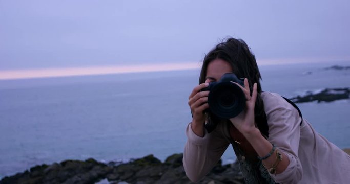 Trendy female photographer holding DSLR up to eye taking landscape photos - medium shot head on
