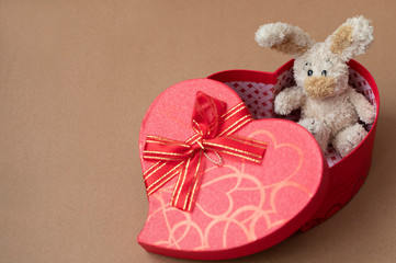 Present for the Valentine's day. Red gift box and red ribbon with tag on brown wooden board background with space for text.