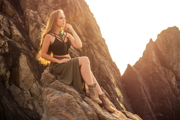 full-length portrait young and beautiful long-haired woman in a stylish skirt and top posing on the rocks beach .feathers dreadlocks in hair and makeup boho brown style dress fashion shoes boots