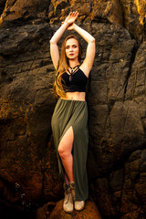 portrait of stylish elegant redheaded chestnut blonde young girl in indie bohemian bo-ho style clothes black stylish top.boho woman long hair,makeup and green feathers in head on the rocks by the sea