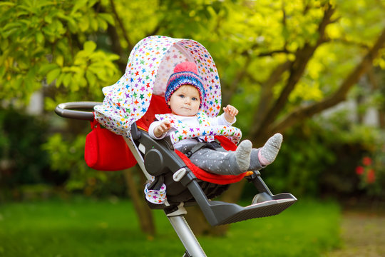 Cute healthy little beautiful baby girl with blue warm hat sitting in the pram or stroller and waiting for mom. Happy smiling child with blue eyes. baby daughter going for a walk with family