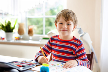 Happy smiling little kid boy at home making homework at the morning before the school starts....