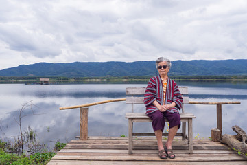 Portrait of elderly woman wearing sunglasses sitting side the lake.