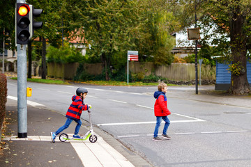 Two little schoolkids boys running and driving on scooter on autumn day. Happy children in colorful...