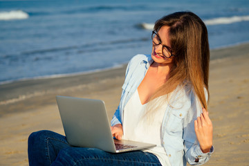 woman in stylish glasses using laptop freelancing on the tropical paradise beach. Girl freelancer...