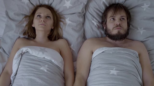 Embarrassed Couple is going to have Sex, but are Shy and do not know what to do. Top view of bearded Man and Woman for the first time together in Bed.