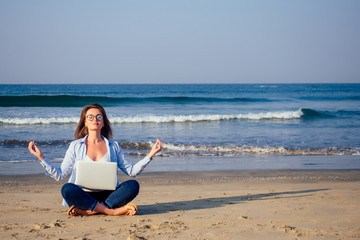 Young calm woman in glasses with laptop freelancing on the tropical paradise beach. Girl freelancer sitting in a summer sand on the seashore dream remote work indian ocean background copyspace