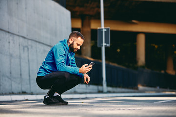 Young Caucasian bearded sporty man with short hair in sportswear crouching on the street and...