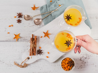Two high glasses with colorful hot sea buckthorn tea with cinnamon sticks, anise stars and fresh sea buckthorn berries