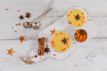 Two high glasses with colorful hot sea buckthorn tea with cinnamon sticks, anise stars and fresh...