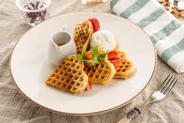 Fresh heart shaped waffles with ice cream and syrup served on the table