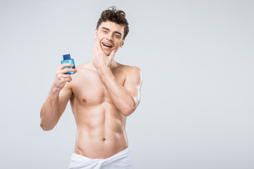 Fototapeta premium happy shirtless man holding bottle with cologne, isolated on grey