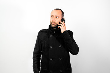 Middle-aged man with overcoat listens attentively to a conversation on his mobile phone, isolated on white.