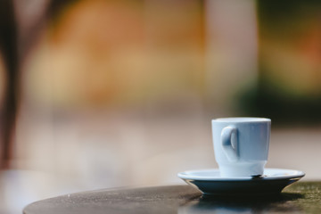 Empty white coffee cup on the wooden table of an outdoor bar, negative space for text.
