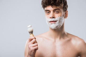 handsome man holding brush with shaving foam, isolated on grey