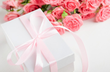 White gift box with a pink ribbon and a bouquet of roses on a white background. A gift for Valentine's Day, birthday, women's day