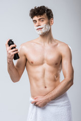 Fototapeta premium handsome shirtless young man holding bottle with shaving foam, isolated on grey