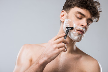 handsome caucasian man foam on face shaving with razor, isolated on grey