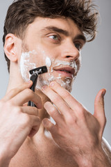 handsome man foam on face shaving with razor, isolated on grey