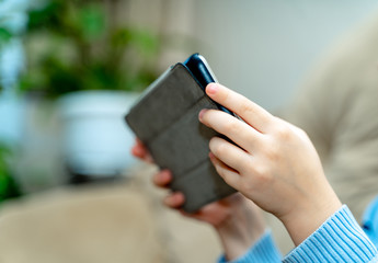 Hands of a boy holding tablet and playing on it against blurry background. Digital tablet in a grey cover in the hands. Close-up