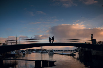 Silhouette of romantic couple walking holding hands on the bridge in the evening. Beautiful sky