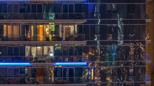 Glowing windows in multistory modern glass and metal residential building light up at night timelapse.