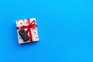 Car key on paper gift box with red ribbon bow and heart on blue table background. Holidays present top view concept