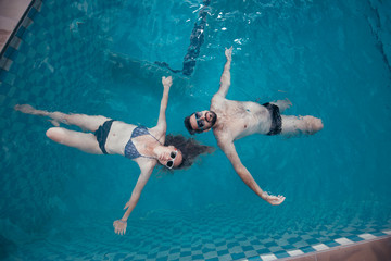 A young pair of lovers swims in the pool. Newlyweds relaxing in the water in the outdoor pool