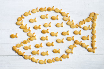 Big fish eats little fish abstract concept illustrated with small crispy cookies on white wooden...